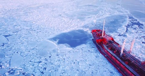 Close aerial view of the ship slowly moving through ice floes. Flying above the Eastern Bosphorus strait. Vladivostok, Russia. Evening