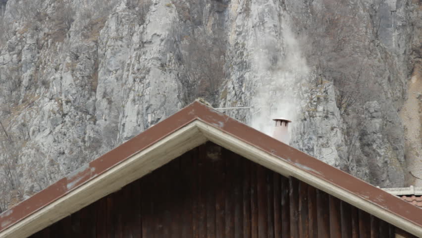 Chalet typical house chimney smoke with mountain rock in background