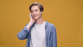 Young happy boy standing isolated over yellow background talking by phone