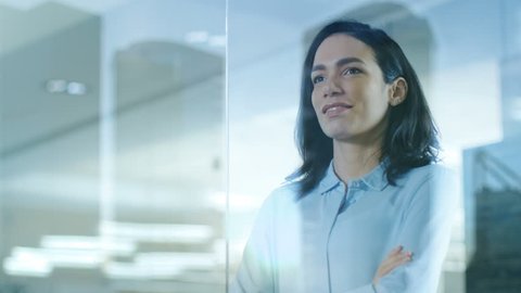 Beautiful Female CEO in Her Office Looks out of the Window on a Big City. Strong Independent Woman with Big Accomplishments Behind and Ahead of Her. Shot on RED EPIC-W 8K Helium Cinema Camera.