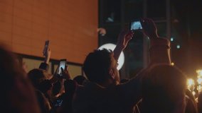 Group of people during concert or light performance on art show use smartphones to film and photograph art visuals to share on social media channels, mass behavior of crowd