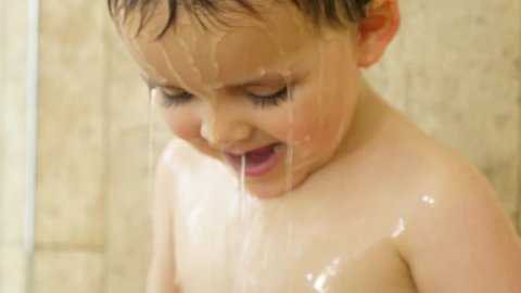 A slow motion shot of a cute little toddler has fun playing and splashing in a shower at his home