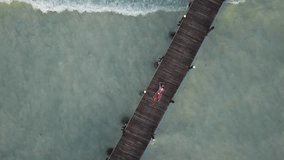 Aerial: the girl lies on a wooden bridge. Waves on the background