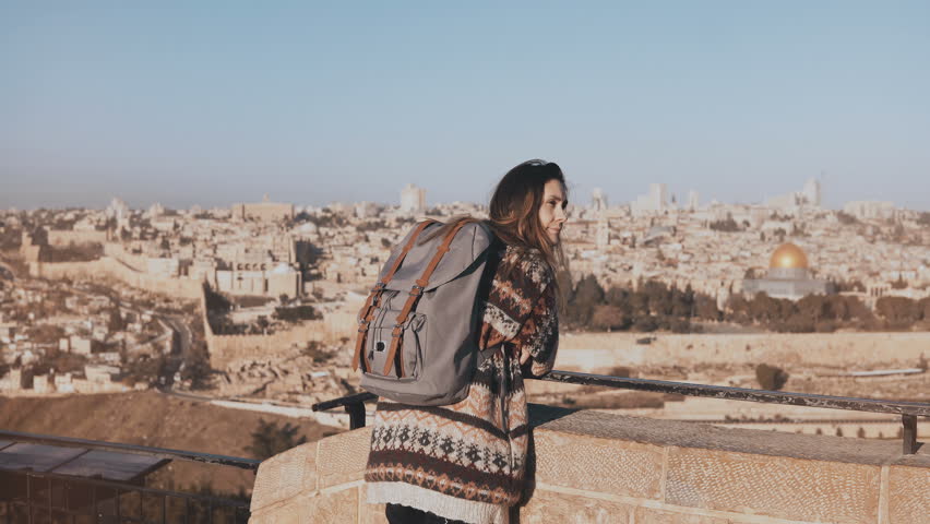 Young girl with backpack enjoys Jerusalem panorama. Thoughtful European tourist looks at ancient old town in Israel. 4K.