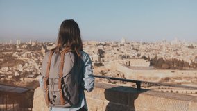 Tourist girl takes photos of old town Jerusalem. Girl with backpack walks to skydeck edge. Capturing moments. Israel 4K.