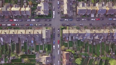 Aerial drone lifestyle concept flying over a street lined with British terraced houses during the golden hour as the sun is setting. Cross roads, a church and people walking and playing feature.