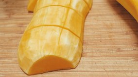 Closeup shot of a woman chopping butternut squash on a wood cutting board in 4k. Female chef uses a kitchen knife to slice the gourd. The recipe video shows step by step of making a vegetable soup.