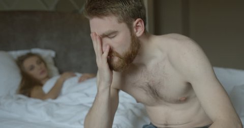 The depressed ginger head man is worrying about problems in bed while his sad disappointed blonde girlfriend in thong is leaving the room.