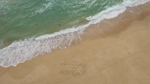 Slow aerial descend over beautiful ocean coastline showing welcome to Australia words written on beach sand