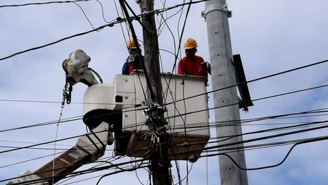San Pablo City, Laguna, Philippines - February 26, 2018: Electrical Workers On Telehandler With Bucket installing High tension wires on high concrete post. Underside view low angle