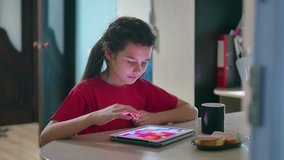 girl teen is eating sandwich plays in a tablet draws on a online game. girl child social media indoors tablet internet drinking tea slow motion video