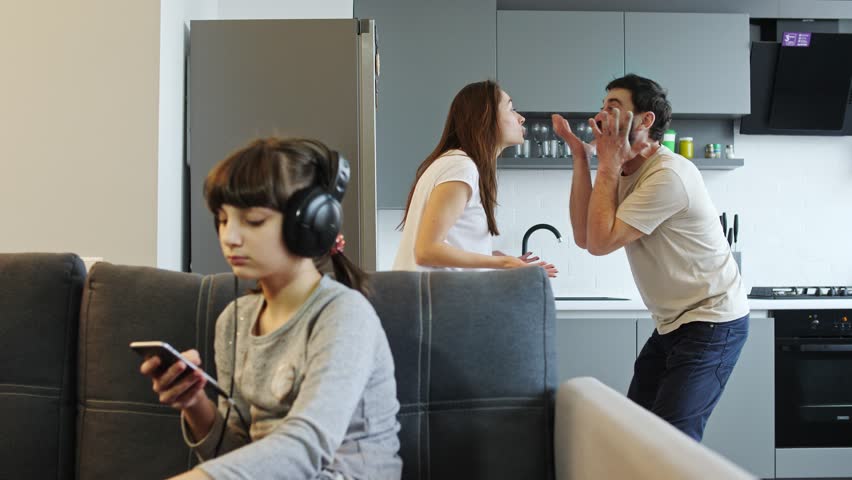 Girl listen music on headphones, while her parents fight at home in the kitchen