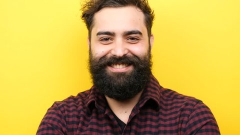 Happy smiling long bearded hipster winking silly on yellow background