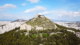 Aerial birds eye view video taken by drone of Lycabettus hill and iconic Saint George chapel on top with beautiful scattered clouds, Athens historic center, Attica, Greece