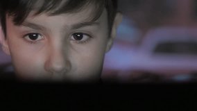 Close up face of Young boy plays video game with laptop in dark room. Double exposure of the game on the face and on the wall.