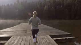 Tracking shot of a young woman running on lake pier and stops, early morning jogging, fog on water surface, People travel sport healthy lifestyle concept.