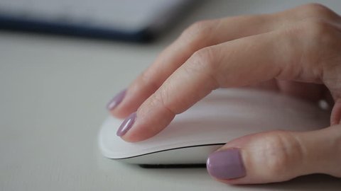 Woman is holding white stylish mouse by her hand, close up. Lady is working on computer and using brand-new device to cooperate with the machine. Female office worker is scrolling the pages by her