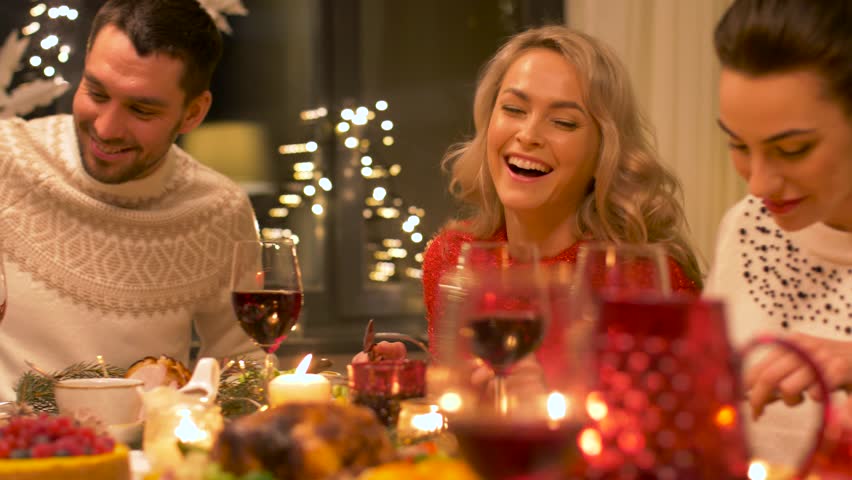 Holidays and celebration concept - happy friends having christmas dinner party at home and eating and drinking wine | Shutterstock HD Video #1008023074