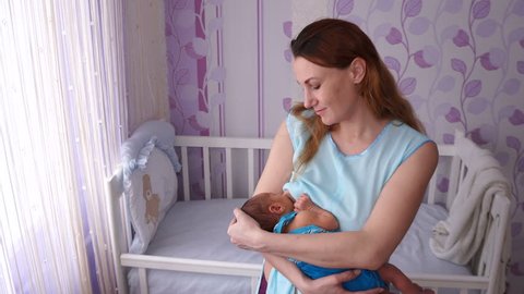 Young mother breast feeding newborn baby in the children's bedroom. Lactation.