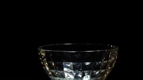 On a black background, cucumbers fall into a glass bowl, slow motion