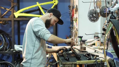 A man bike mechanic with a beard assembles a mountain bike in his workshop.