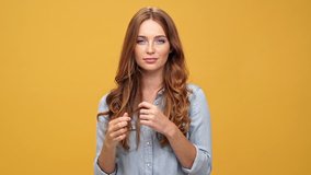 Playful ginger woman in denim shirt showing grimaces and looking at the camera over yellow background