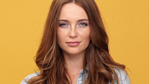 Close up of Smiling ginger woman in denim shirt keep secret and looking at the camera over yellow background