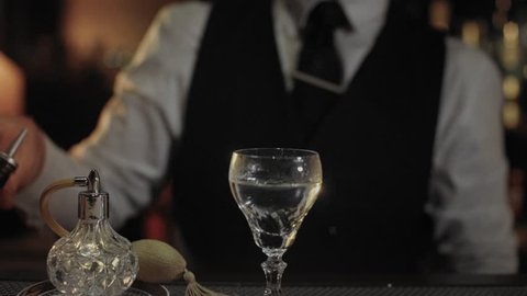 Professional bartender at expensive and luxurious unique bar, prepares fancy drink or cocktail, dry martini in vintage glass, uses infusions or insense to add flavor