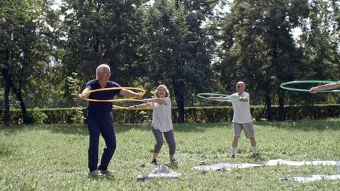 Group of senior people holding hula hoops in front of themselves and performing torso rotation exercises with their trainer