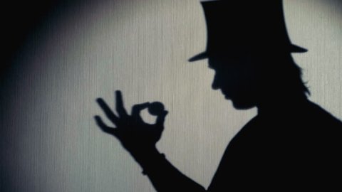Silhouette of magician in a top hat showing a trick.