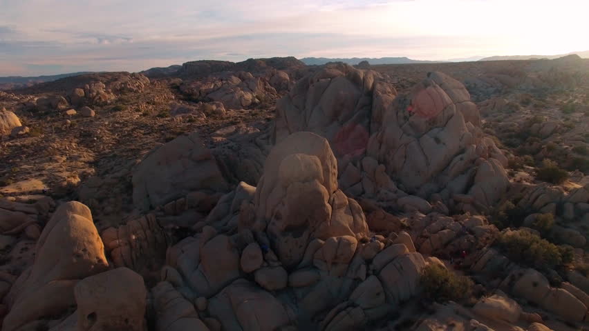Drone flying over rock formations in Joshua Tree National Park tilting down and then back up at sunset