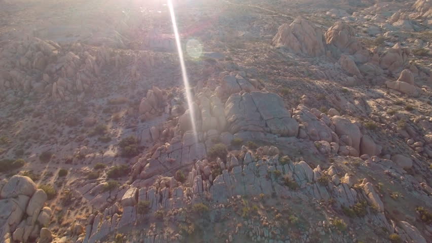 Fast cinematic flyover of rock formations in Joshua Tree National Park with sunset lens flare
