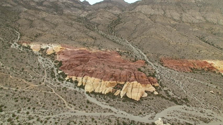 Aerial flying towards a tan and red rock formation in Joshua Tree National Park
