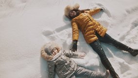 Young mother and little daughter making angels on the snow. Top view with copyspace. Family have fun in sunny winter day outdoors - Powered by Shutterstock - Get 15% off with code: PIKWIZARD15
