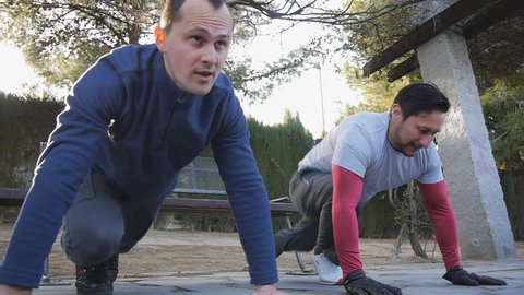 Workout with personal trainer outdoors. Two male athletes doing plank knee to elbow exercises together in a park as part of a workout routine