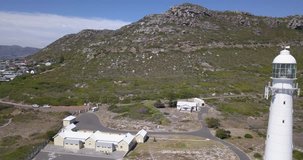 4K high quality aerial video sunny day view of historical Slangkop lighthouse built in 1914 and Kommetjie town in the background near beach at sea shore in Western Cape near Cape Town, South Africa