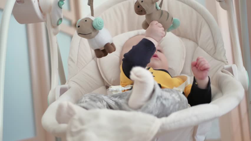 Newborn baby boy swinging on electric swing and playing toys Royalty-Free Stock Footage #1008049024