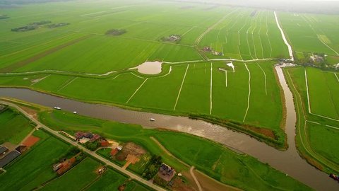 Drone filming Dutch landscape with river, boats, farms and ditches. 4K