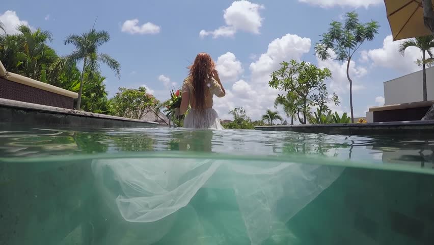 Bride in wedding dress comes to the pool at luxury villa underwater