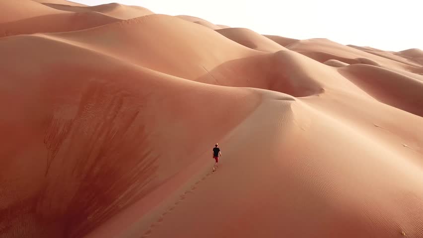 Aerial drone view of a slim man in casual clothes hiking in giant Empty Quarter sand dunes. Abu Dhabi, UAE.