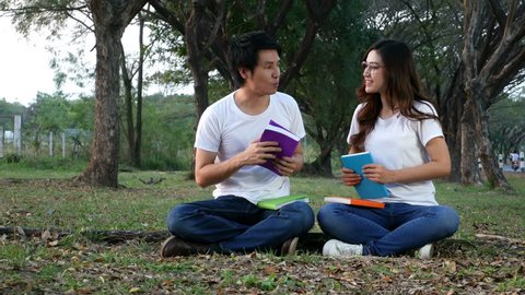4k video of Young man and a woman reading a book in the park. They sit on a green lawn