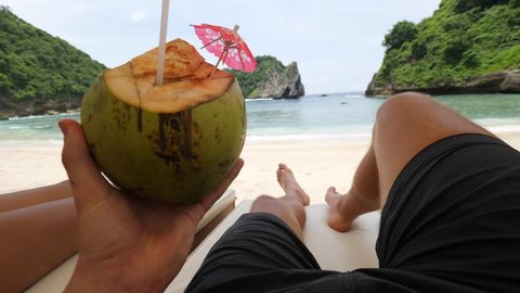 Young Tourist Drinking Young Coconut and Relaxing on Sandy Beach at Tropical Paradise Island. 4K Gopro First Person View. POV. Nusa Penida, Bali, Indonesia.