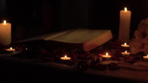 The witch cuts his hand with a ritual knife against the backdrop of a book and a skull by candlelight