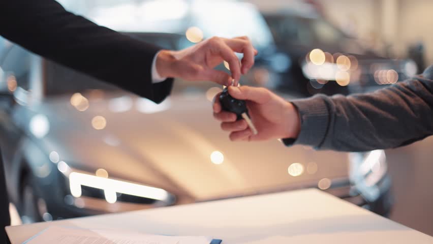 Young man giving keys of car to buyer. Men shaking hands in beautiful car dealership on background of bought cars. Royalty-Free Stock Footage #1008067507