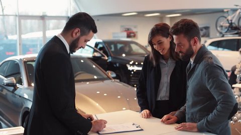 Happy young couple buying new car. Seller of machines and buyer shaking hands, putting in turn signatures in contract. Seller of machines making successful deal.