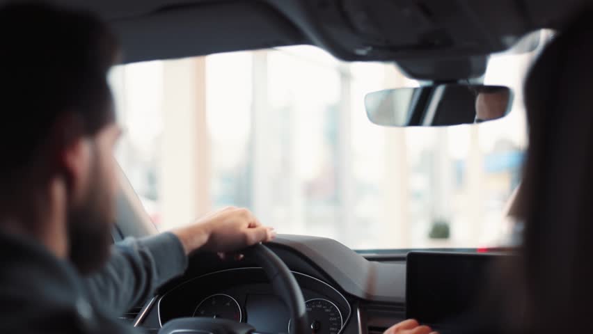 Man sitting at wheel of new car. Young handsome man with beard regulating and looking at rearview mirror. Royalty-Free Stock Footage #1008068107