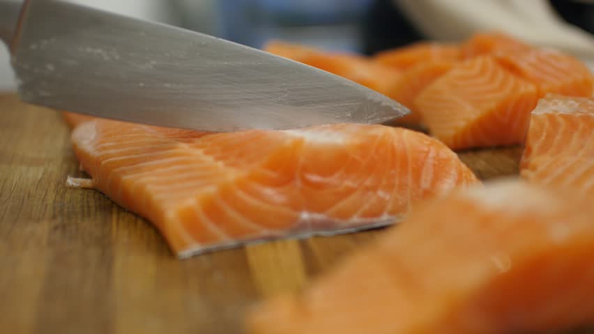 4K close up bokeh shot of a piece of salmon being sliced on a wooden board with a sharp chef