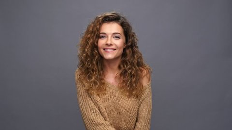 Smiling curly woman in sweater showing silence gesture over purple background
