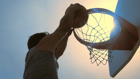 Basketball player scoring slam dunk outdoors in slow motion 