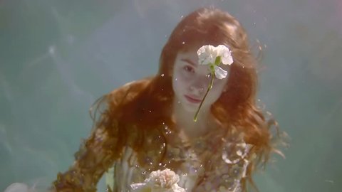 young woman with long red hair underwater like in a fairy tale floats with a bouquet of flowers in her hand